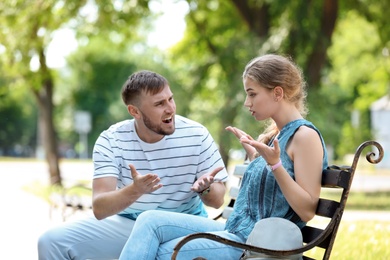 Young couple arguing while sitting on bench in park. Problems in relationship