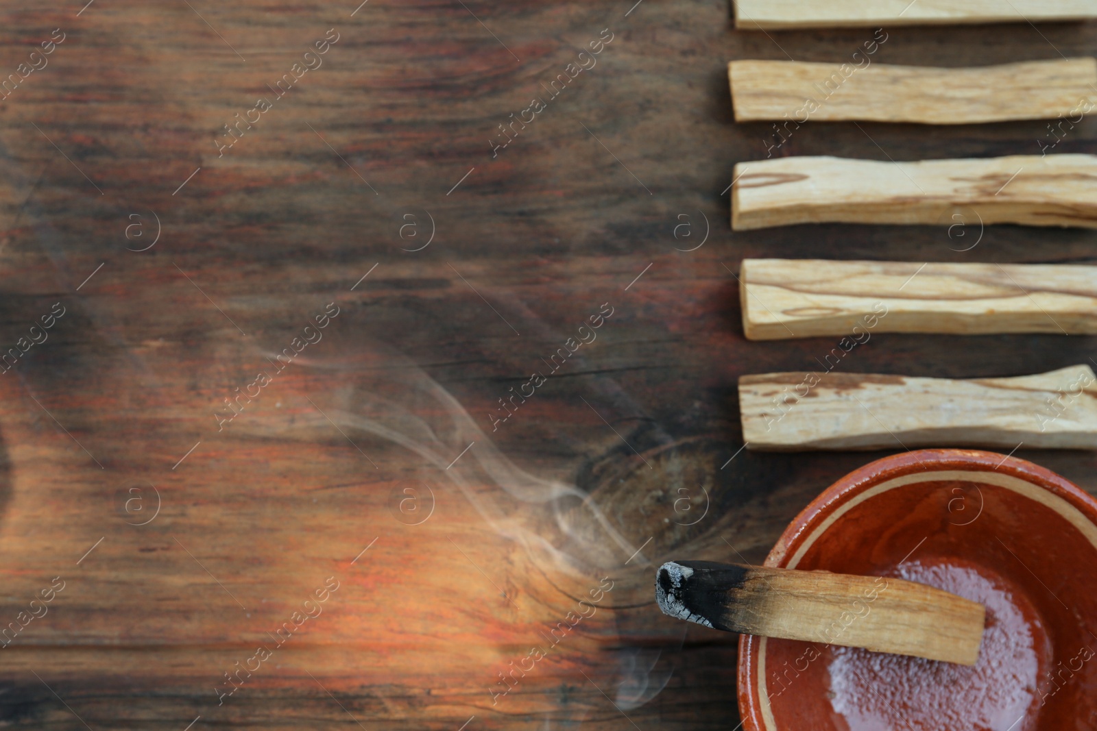 Photo of Palo santo stick smoldering in bowl on wooden table, flat lay. Space for text