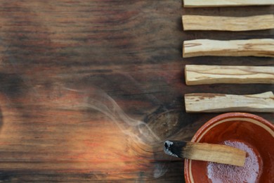 Palo santo stick smoldering in bowl on wooden table, flat lay. Space for text