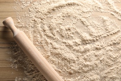 Photo of Scattered flour and rolling pin on wooden table, top view