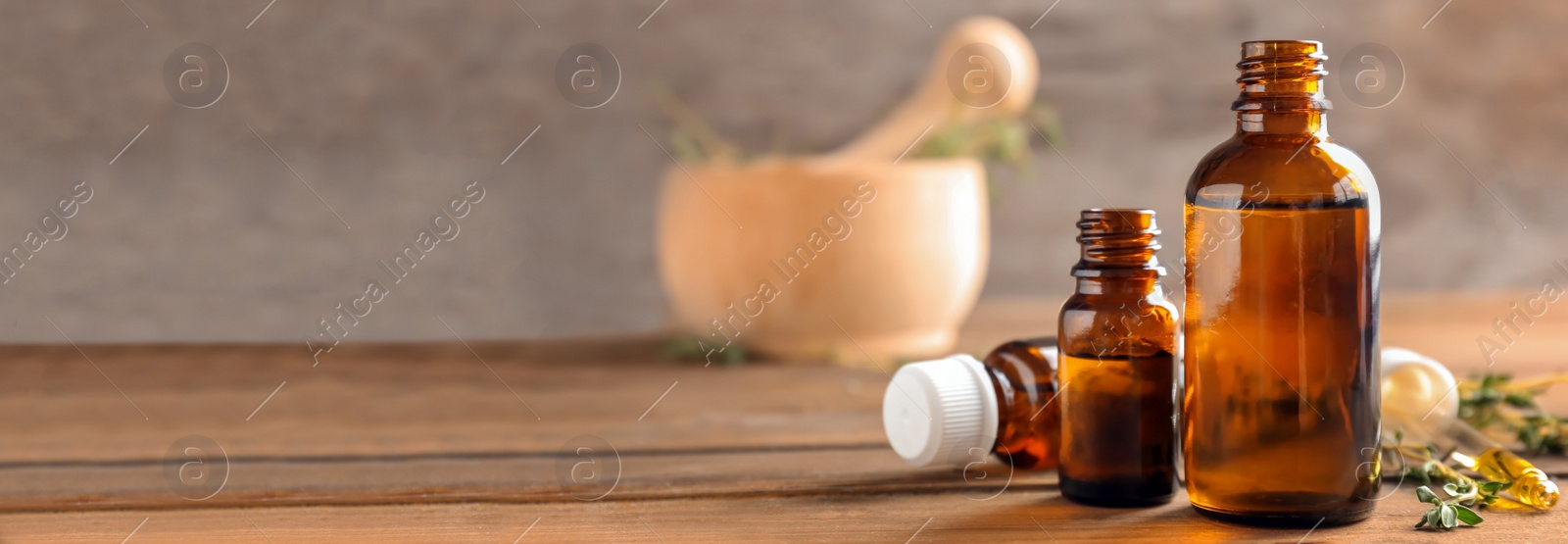 Image of Bottles of essential oil with thyme on wooden table, space for text. Banner design