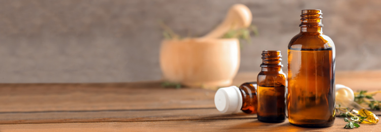 Image of Bottles of essential oil with thyme on wooden table, space for text. Banner design