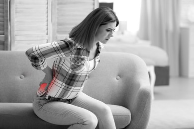 Image of Woman suffering from back pain at home. Black and white effect with red accent