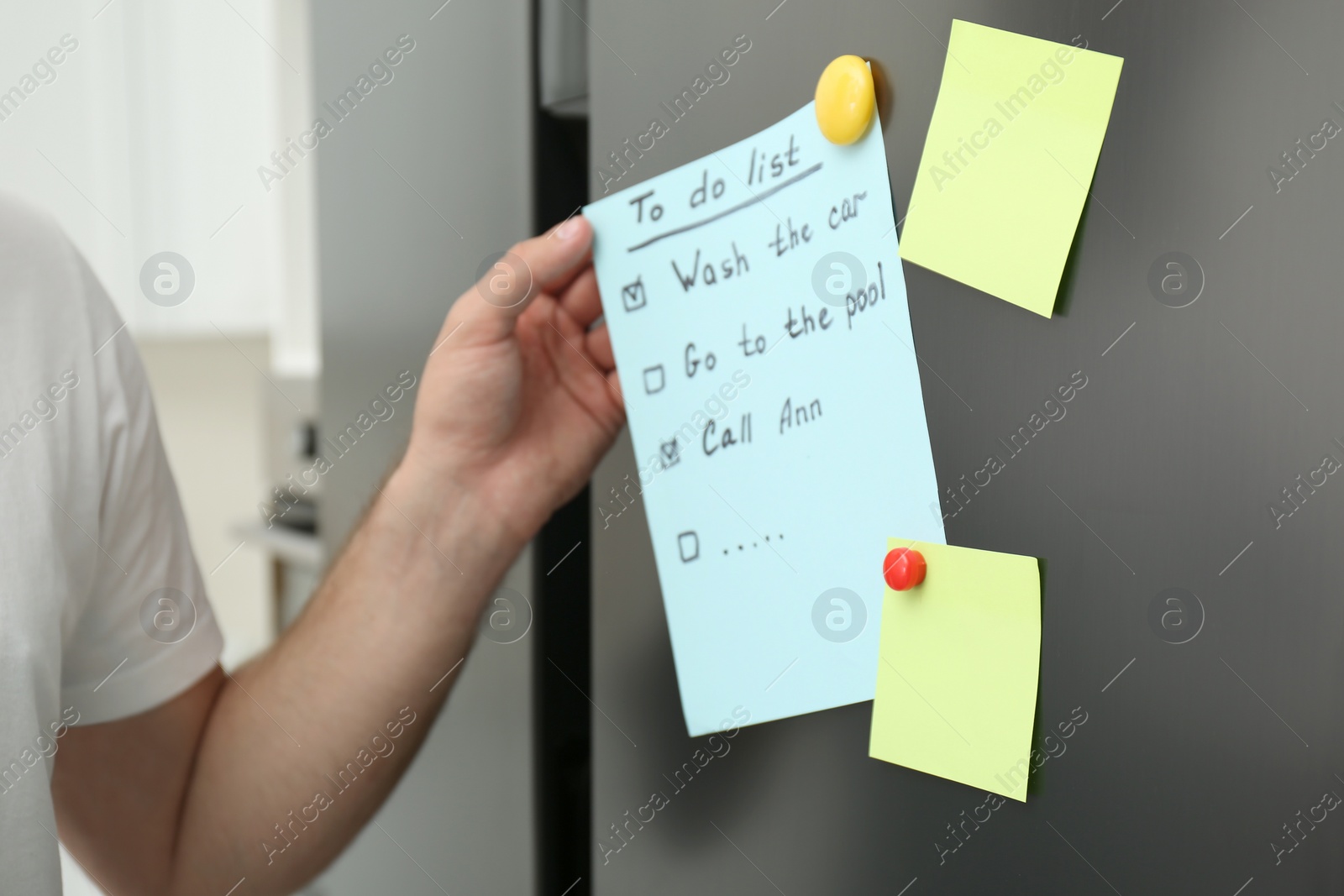 Photo of Man taking to do list from refrigerator door in kitchen, closeup