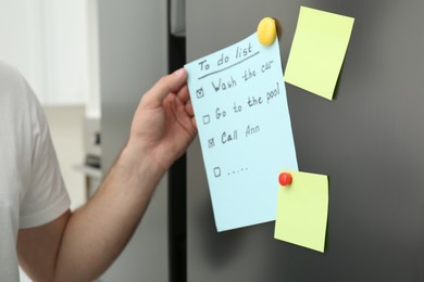 Photo of Man taking to do list from refrigerator door in kitchen, closeup