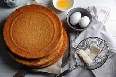 Delicious homemade sponge cake and ingredients on white wooden table, above view