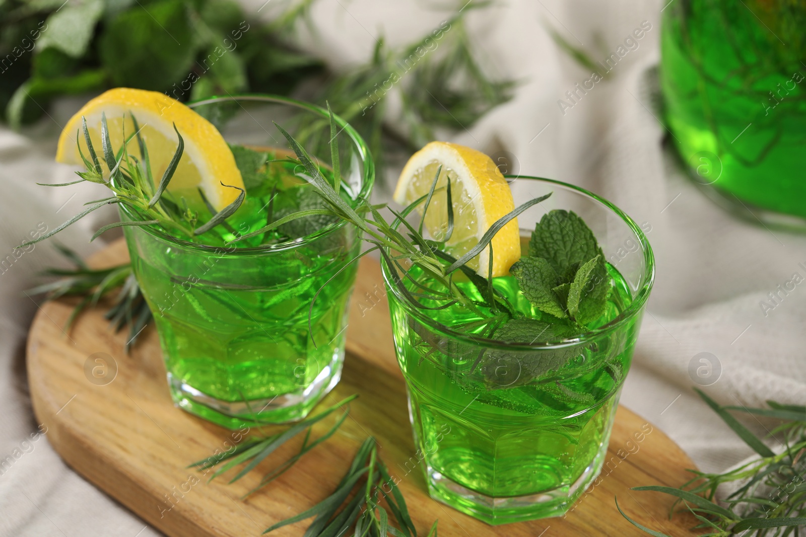 Photo of Glasses of refreshing tarragon drink with lemon slices on tablecloth