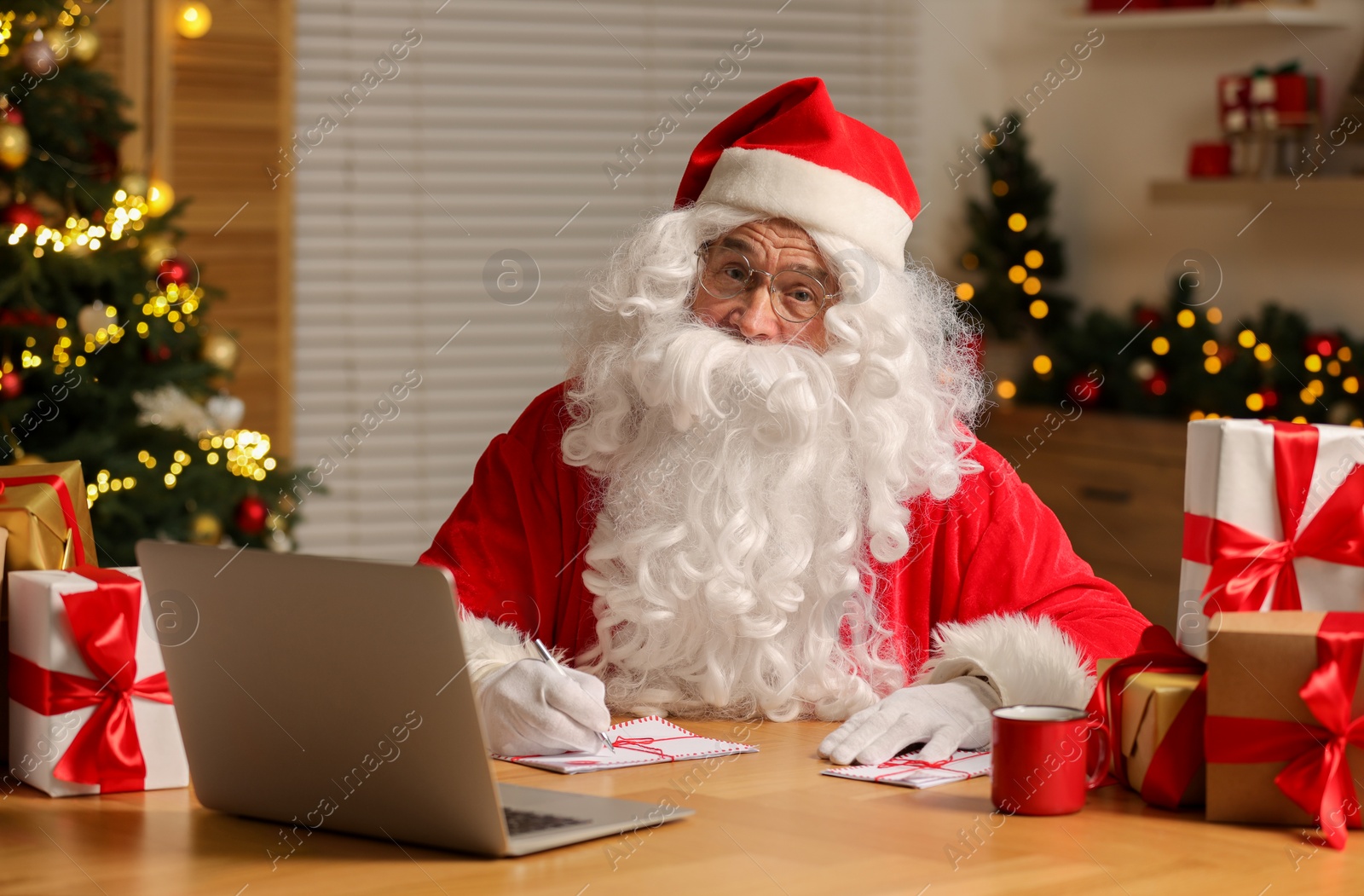 Photo of Santa Claus signing Christmas letters at table in room