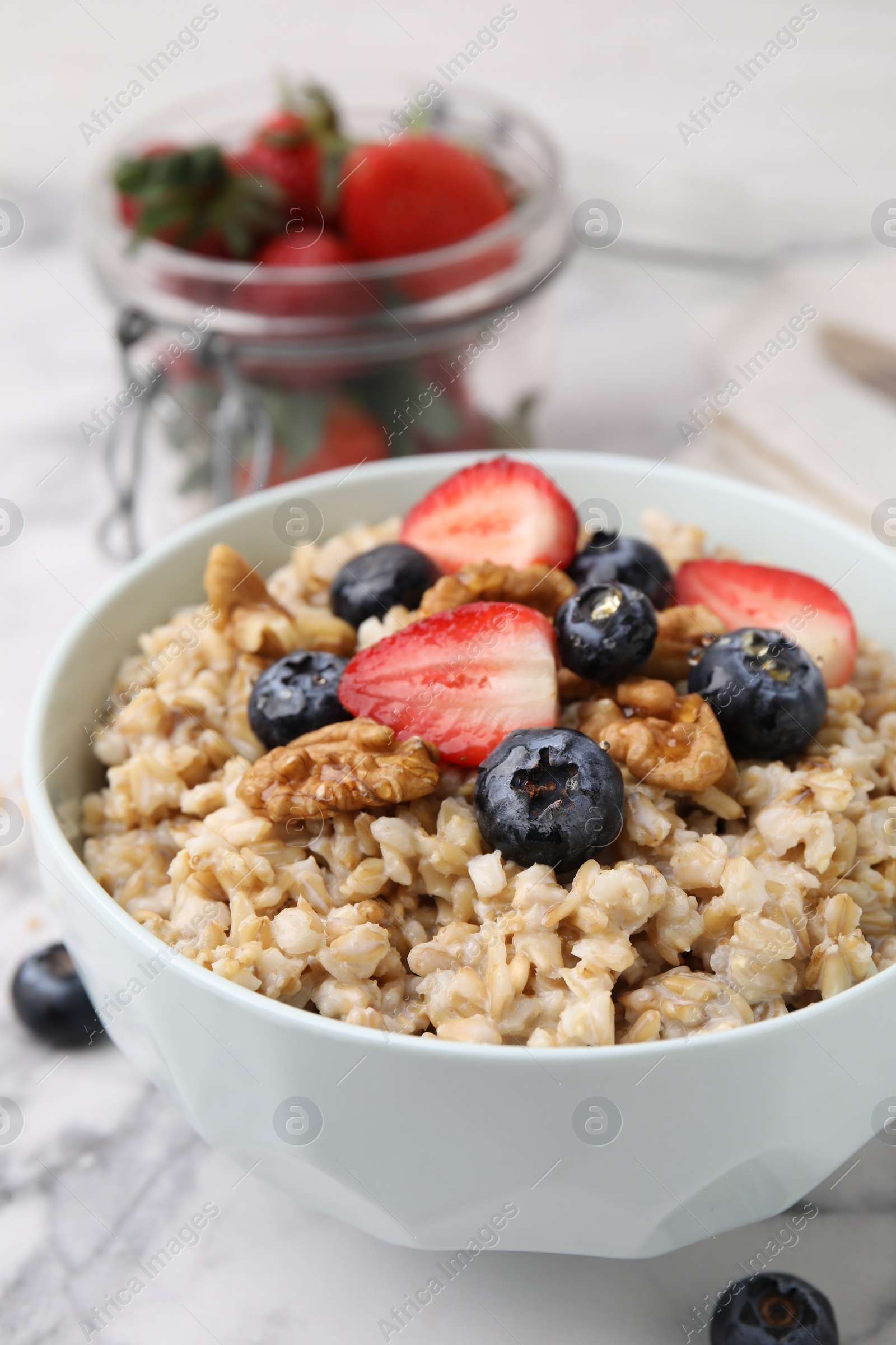 Photo of Tasty oatmeal with strawberries, blueberries and walnuts in bowl on white marble table, closeup