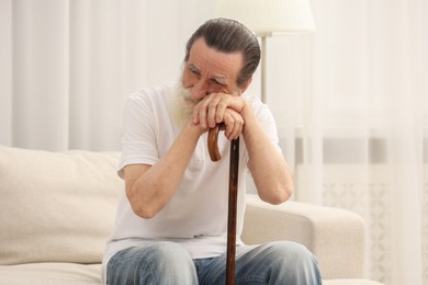 Senior man with walking cane on sofa at home