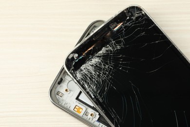 Broken smartphone on light beige wooden background, closeup. Device repair