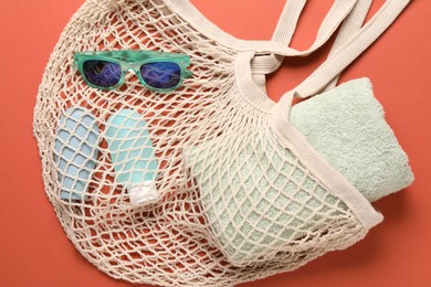 Photo of String bag, sunglasses, cosmetic products and towel on coral background, top view