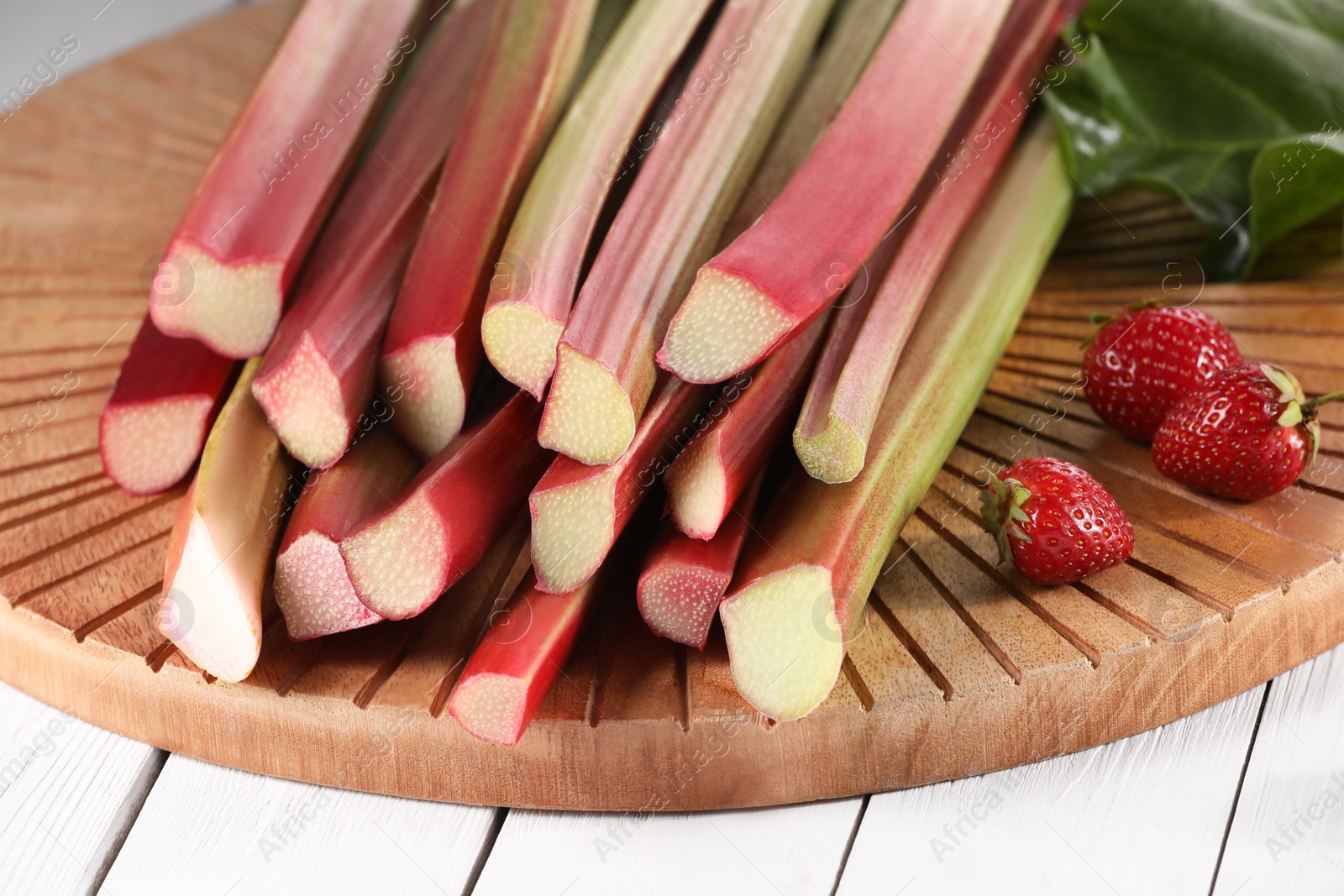 Photo of Cut fresh rhubarb stalks and strawberries on white wooden table, closeup