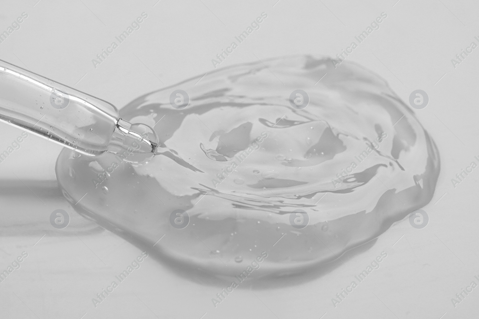 Photo of Dripping facial gel from pipette on white background, closeup