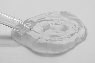 Photo of Dripping facial gel from pipette on white background, closeup