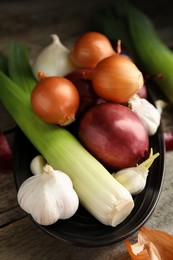 Plate with fresh onion bulbs, leek and garlic on wooden table, closeup