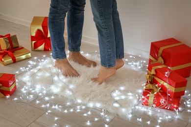 Photo of Young couple standing on rug near Christmas lights and gift boxes, closeup