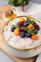 Photo of Delicious barley porridge with blueberries, pumpkin, dates and mint in bowl on table, closeup