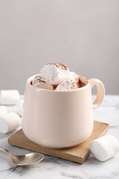 Cup of aromatic hot chocolate with marshmallows and cocoa powder served on white marble table