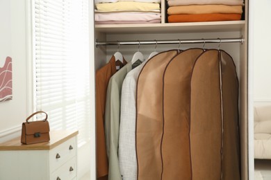 Garment bags with clothes on rack in wardrobe indoors