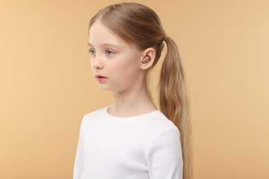 Little girl with hearing aid on pale brown background