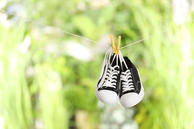 Stylish sneakers drying on washing line against blurred background, space for text