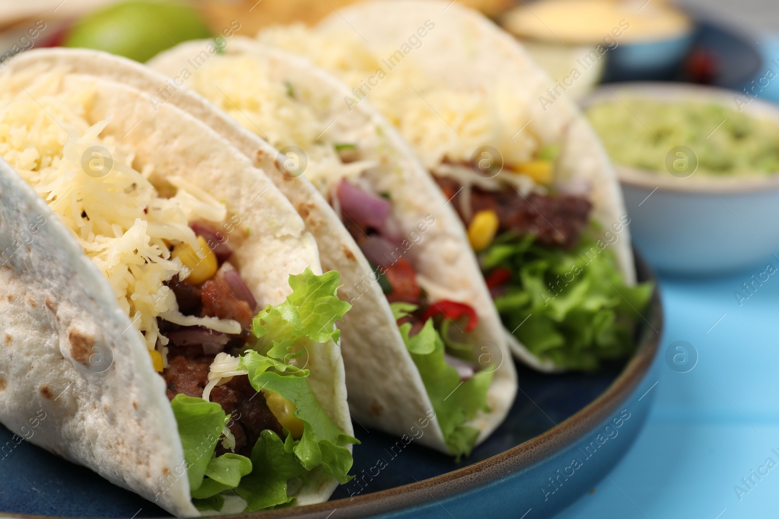 Photo of Delicious tacos with meat and vegetables on light blue table, closeup