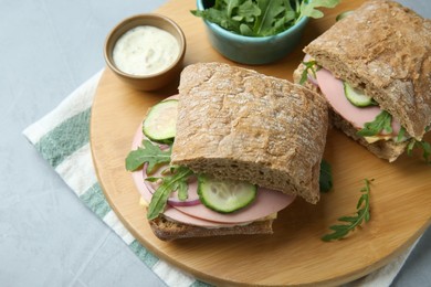 Photo of Tasty sandwiches with boiled sausage, cucumber, arugula and sauce on grey table, closeup