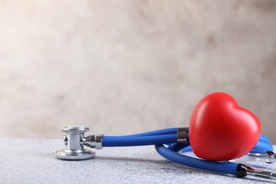 Stethoscope and red heart on grey stone table, closeup. Space for text