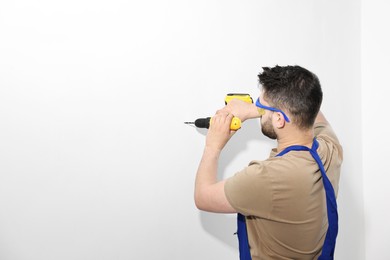 Photo of Young worker in uniform using electric drill indoors. Space for text