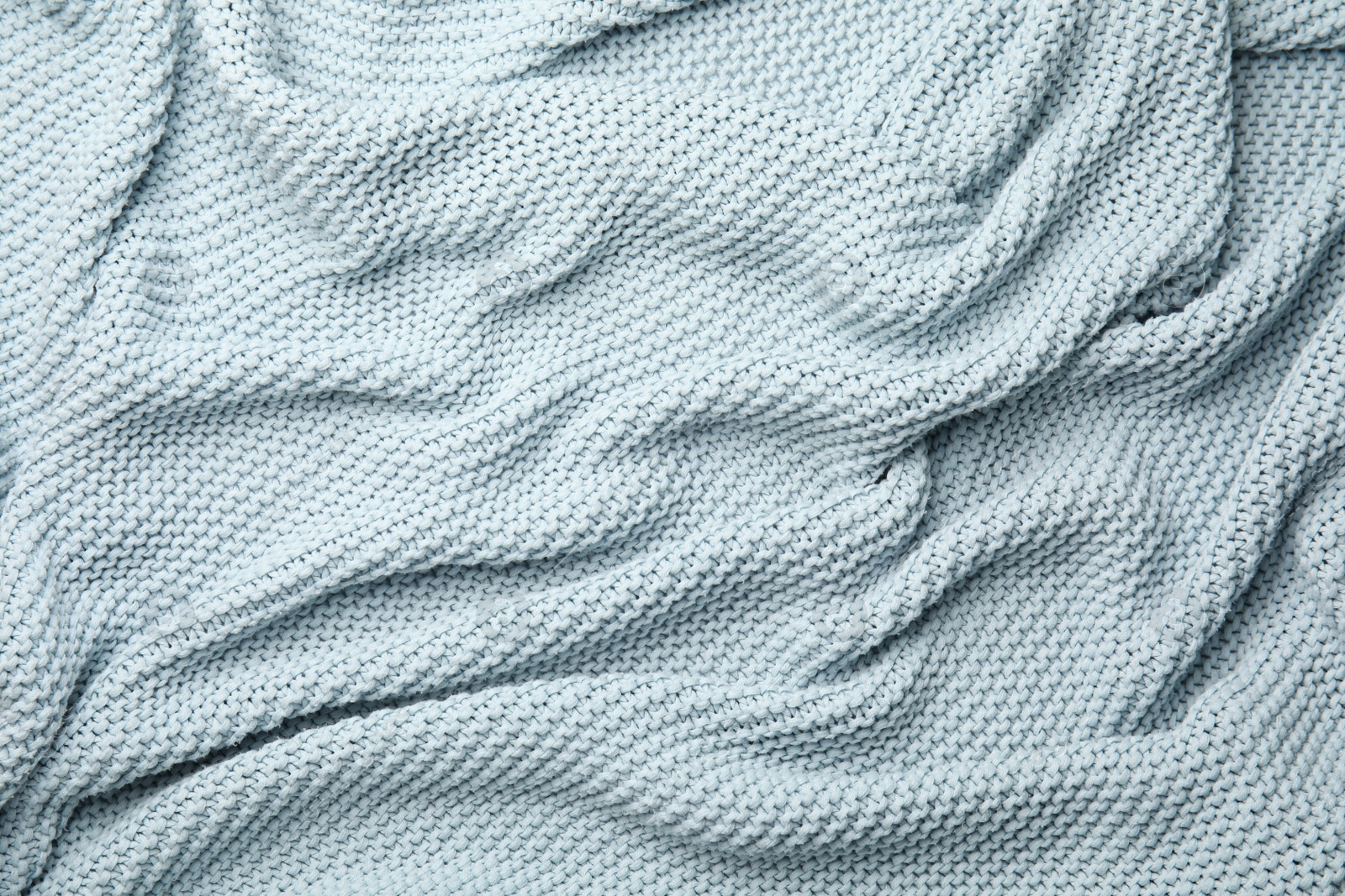Photo of Soft light blue knitted plaid as background, top view