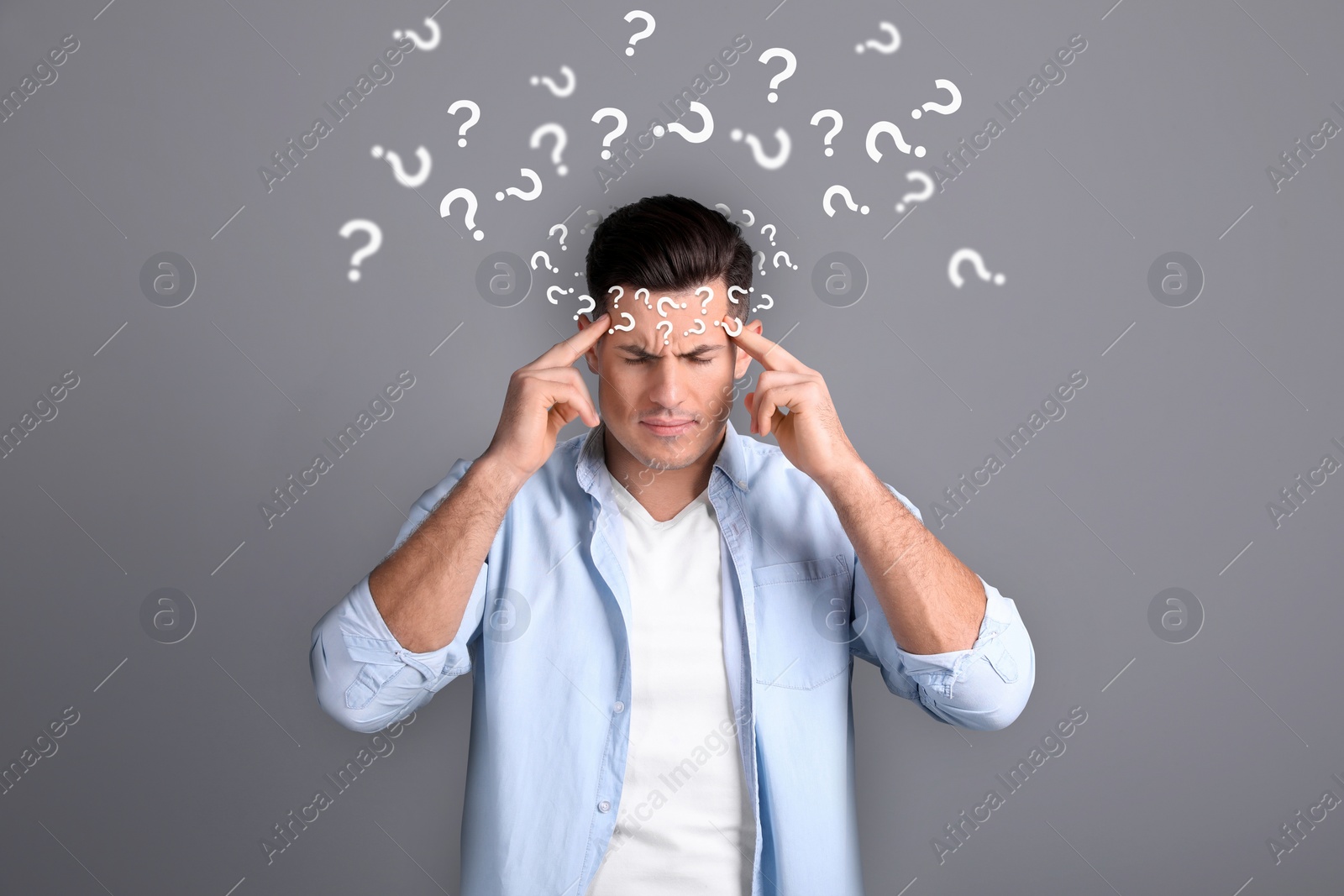 Image of Amnesia concept. Man surrounded by question marks trying to remember something on grey background