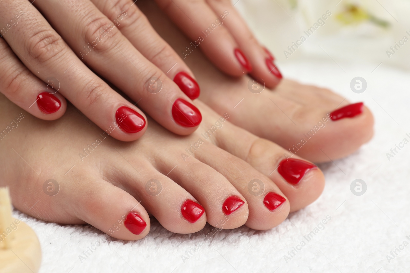 Photo of Woman showing stylish toenails after pedicure procedure and manicured hands with red polish on white terry towel, closeup