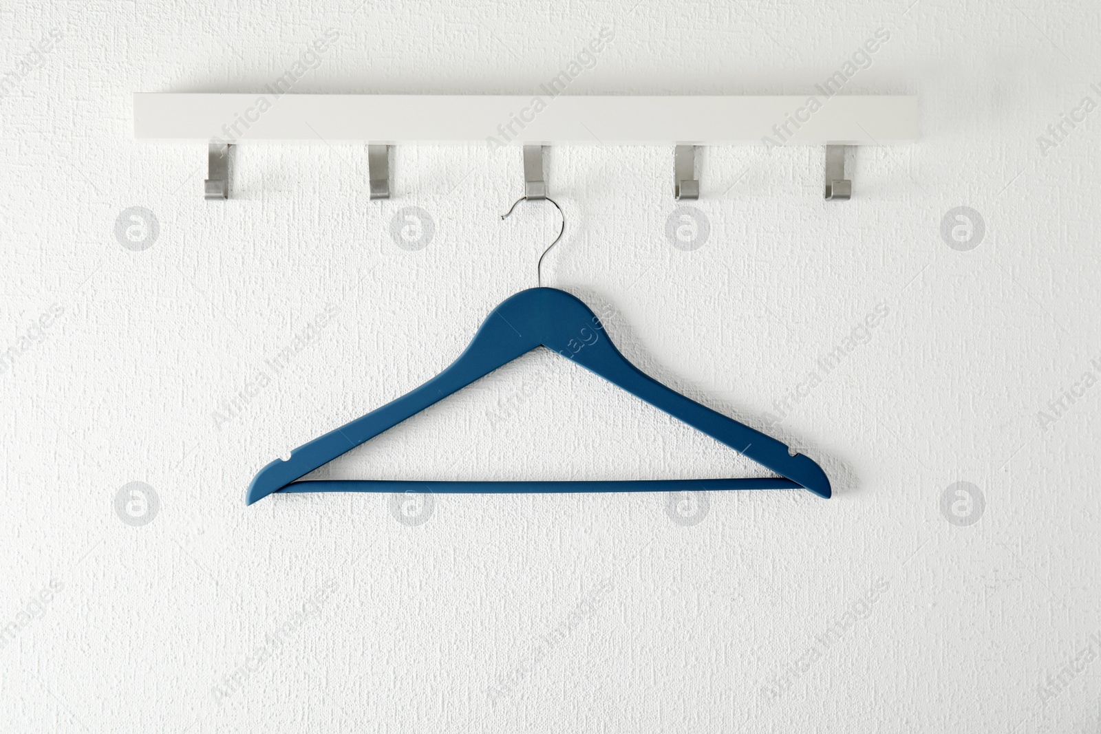 Photo of Rack with empty clothes hanger on light wall. Wardrobe accessory