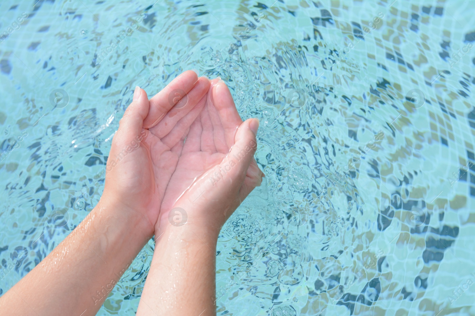 Photo of Girl holding water in hands above pool, closeup. Space for text