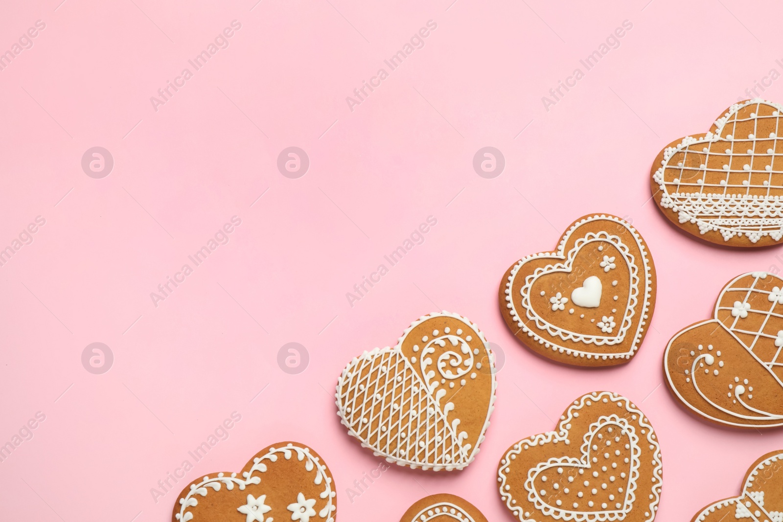 Photo of Gingerbread hearts decorated with icing on pink background, flat lay. Space for text