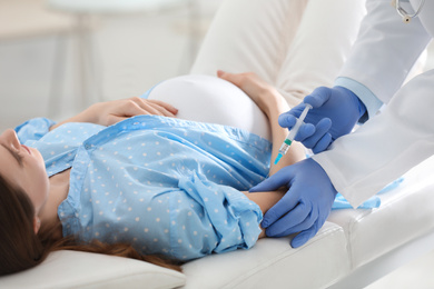 Photo of Doctor giving injection to pregnant woman in hospital, closeup. Vaccination concept