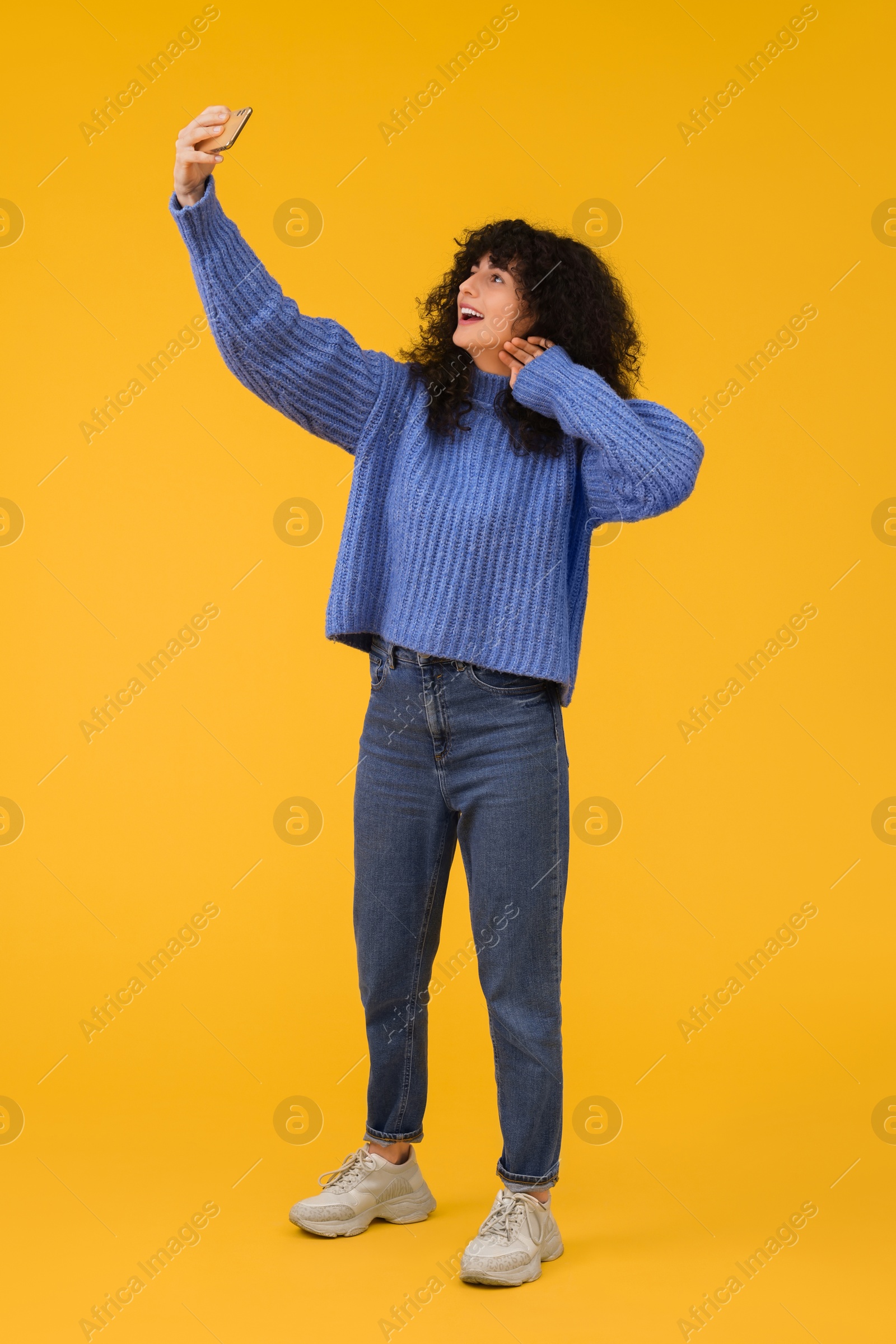 Photo of Beautiful young woman taking selfie with smartphone on orange background