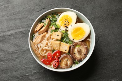 Photo of Noodle soup. Bowl of delicious ramen on black table, top view