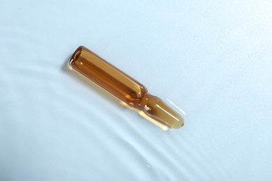 Photo of Skincare ampoule in water on light blue background, top view