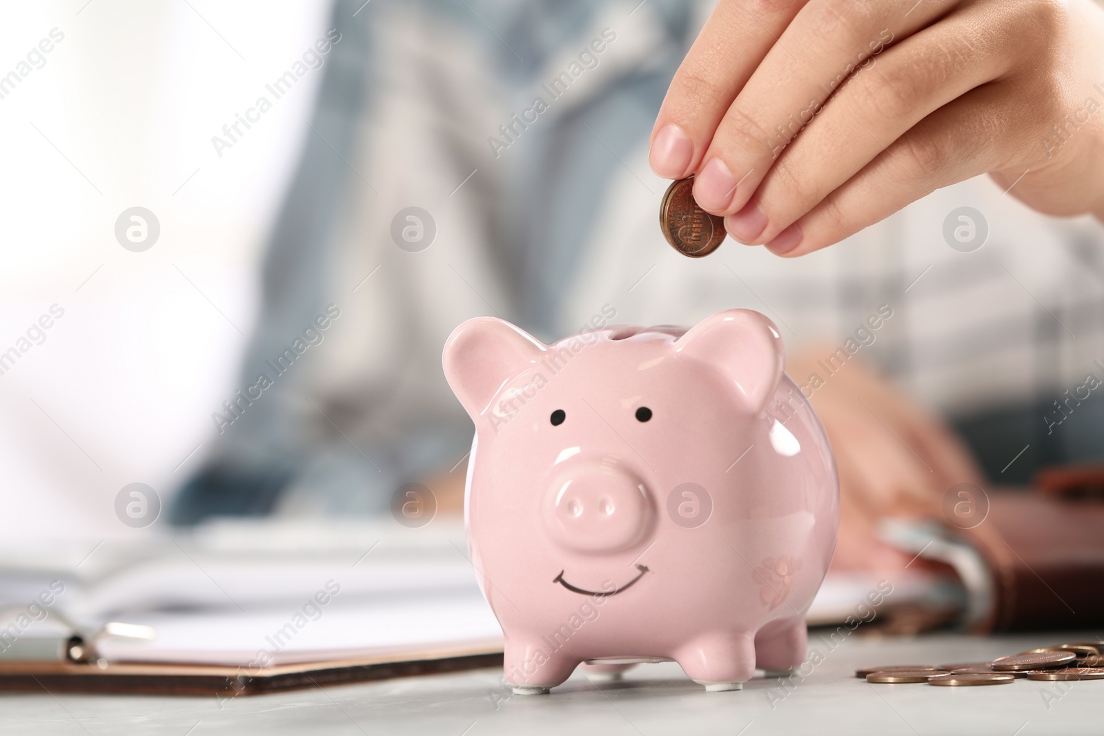 Photo of Woman putting money into piggy bank at table, closeup