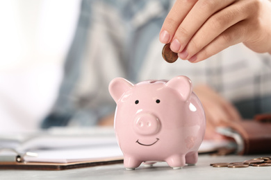 Photo of Woman putting money into piggy bank at table, closeup