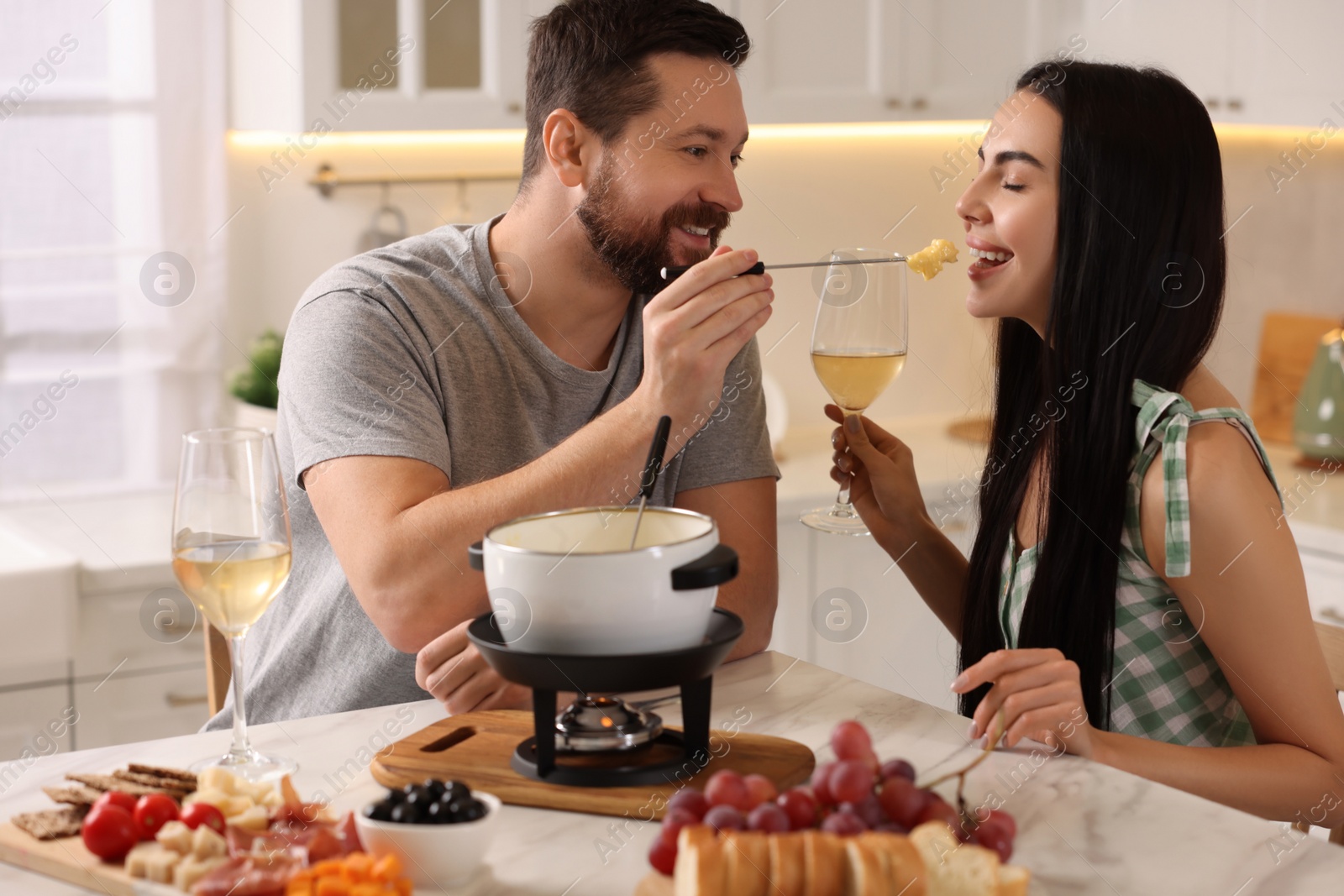 Photo of Affectionate couple enjoying cheese fondue during romantic date in kitchen