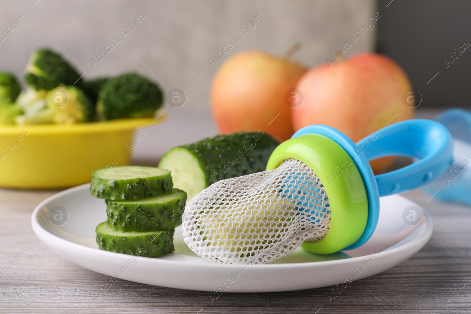 Photo of Nibbler with fresh cucumber on white wooden table. baby feeder