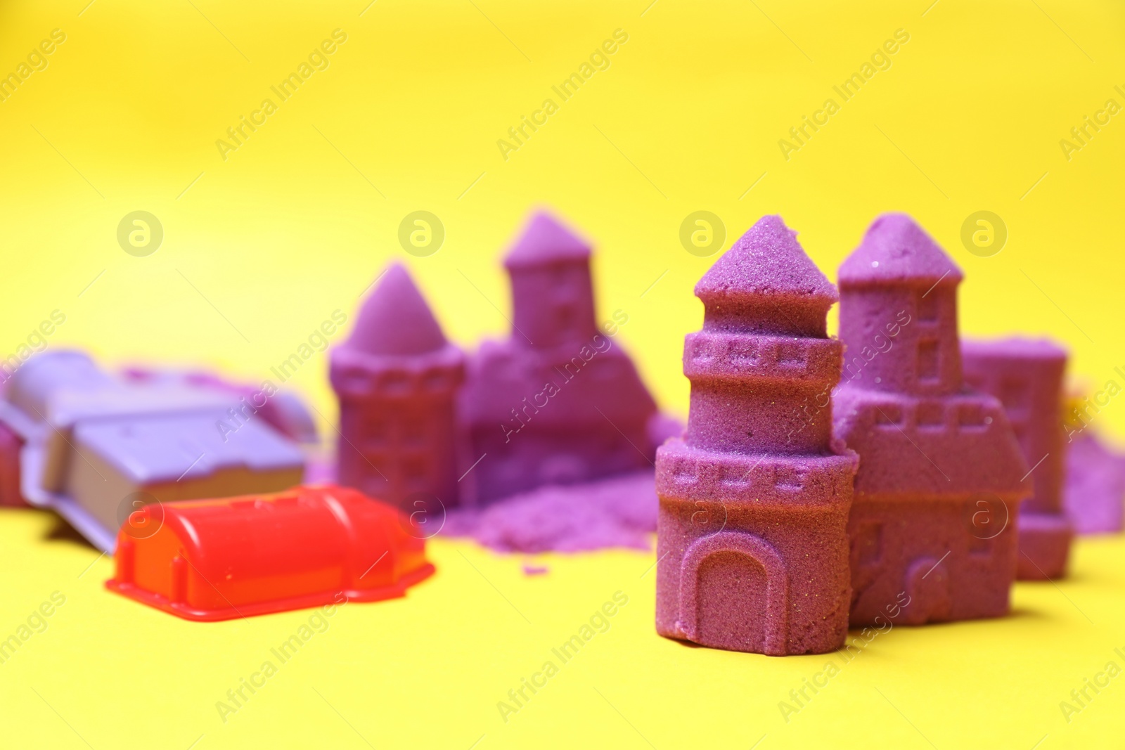 Photo of Castle figures made of kinetic sand and plastic toys on yellow background, closeup