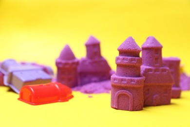Photo of Castle figures made of kinetic sand and plastic toys on yellow background, closeup