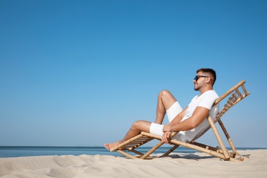 Young man relaxing in deck chair on sandy beach