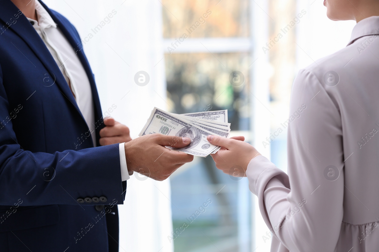 Photo of Man giving bribe money to woman indoors, closeup