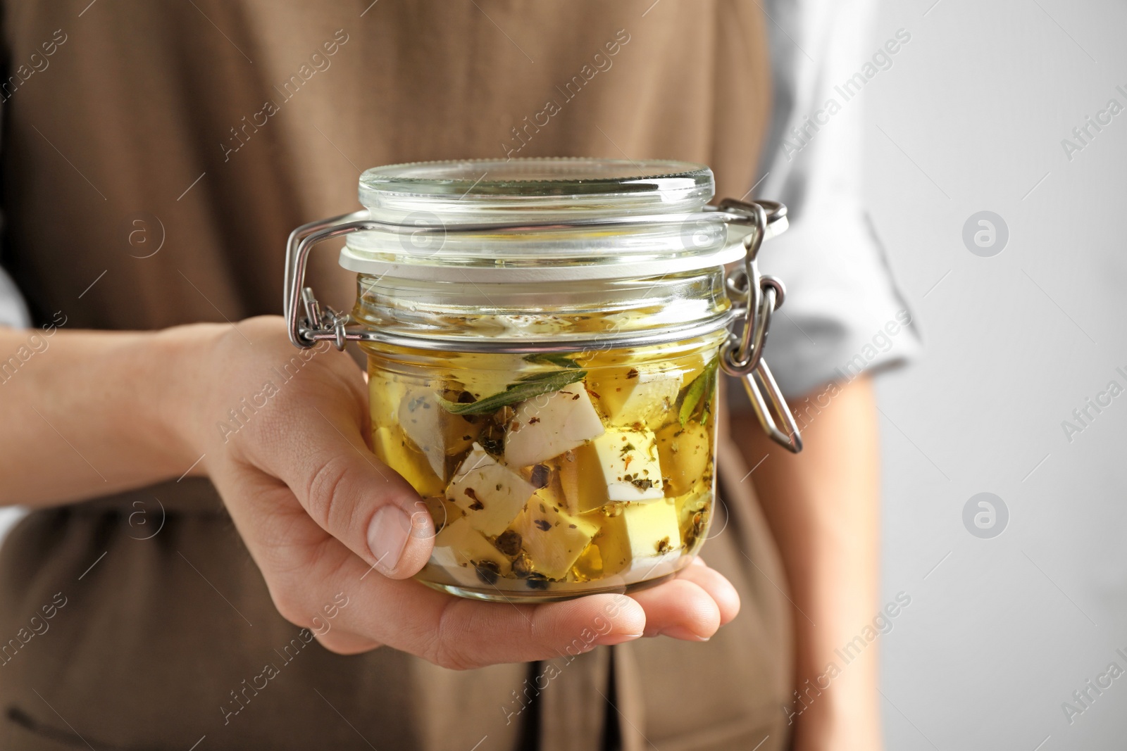 Photo of Woman holding jar with pickled feta cheese on grey background, closeup