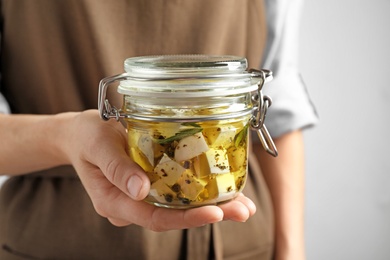 Photo of Woman holding jar with pickled feta cheese on grey background, closeup